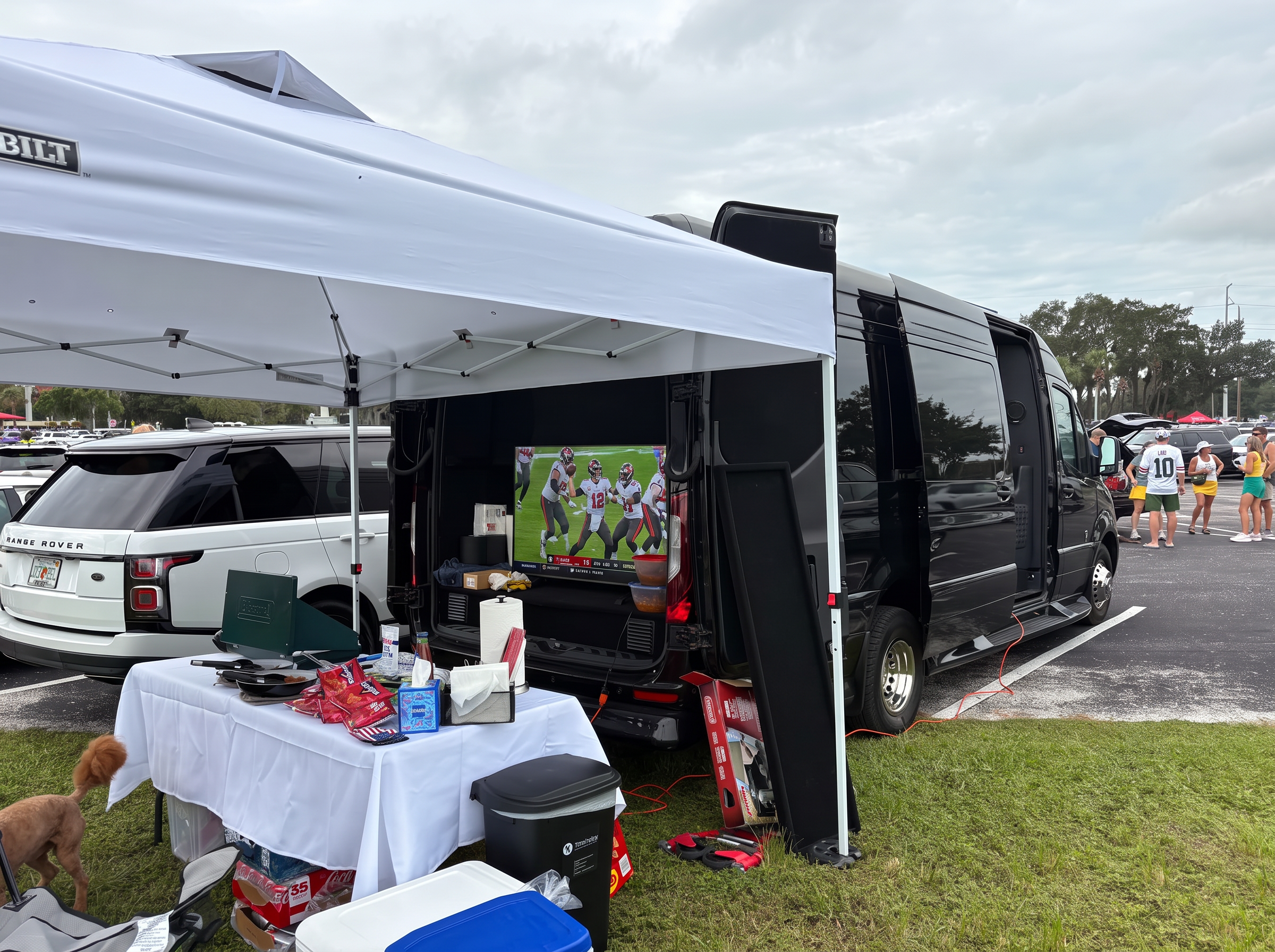 The black Sprinter set up for a stadium tailgate with canopy, TV, grill and coolers